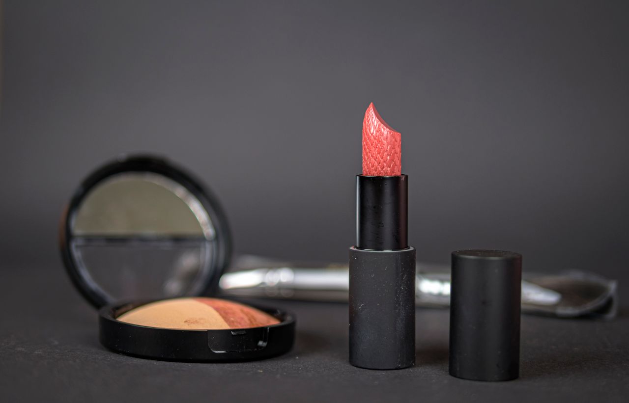 Black lipstick and blush with compact on dark background, showcasing elegant makeup essentials.