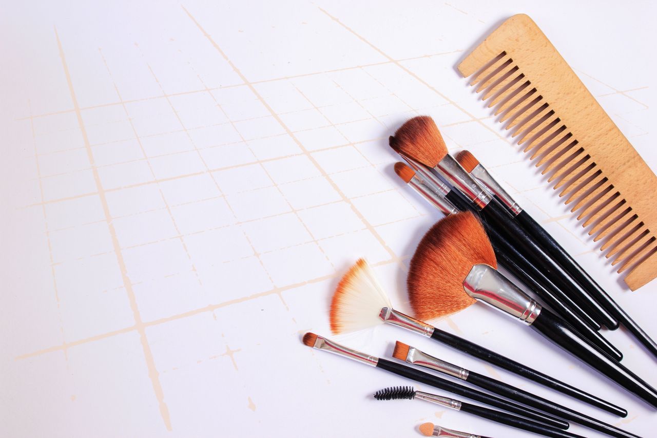Flat lay of various makeup brushes and a wooden comb on a white grid-patterned background.