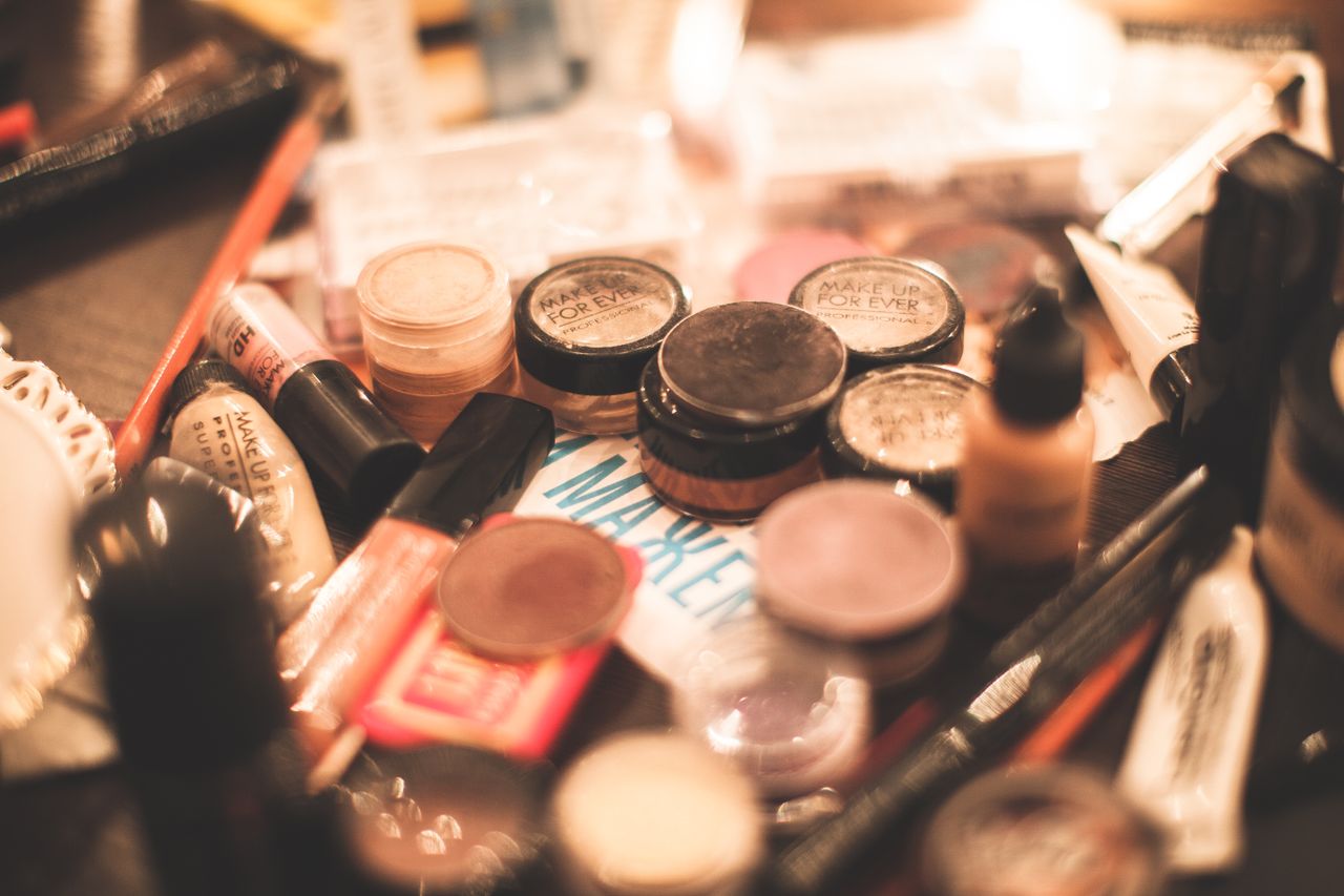 A vibrant collection of cosmetics including eyeshadows, lipsticks, and brushes on a table.